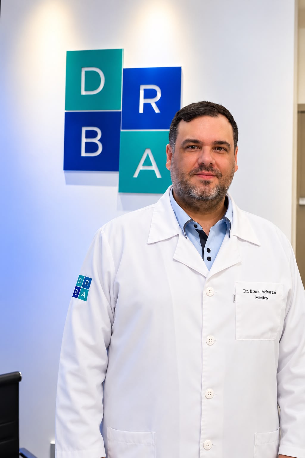 Dr. Bruno Acharezzi de jaleco branco com o logotipo da Clínica DRBA ao fundo